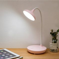 a pink table lamp sitting on top of a wooden desk next to a tablet computer