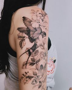 a woman's arm with flowers and a bird on the back of her shoulder