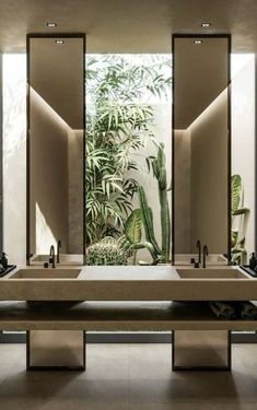 a bathroom with two sinks, mirrors and plants on the wall behind them in front of an open door