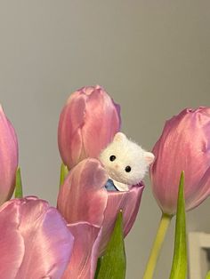 a white mouse sitting in the middle of pink tulips