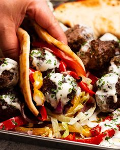 a tray filled with meatballs and veggies covered in white sauce being held by someone's hand