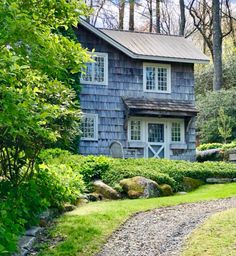 a house in the woods surrounded by trees and bushes with a gravel path leading to it