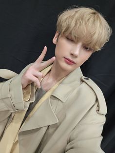 a young man in a trench coat making the peace sign with his hand while sitting down