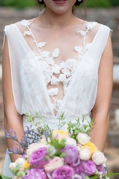 a woman in a white dress holding a bouquet of purple and yellow flowers on her wedding day