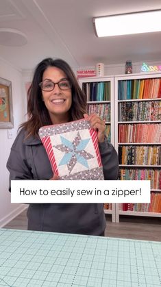 a woman holding up a quilt in front of a book shelf with books on it