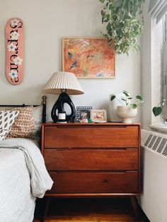 a bedroom with a bed, dresser and lamp on the side table in front of a window