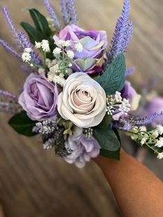 a bridal bouquet with purple flowers and greenery on the wrist, in front of a wooden background