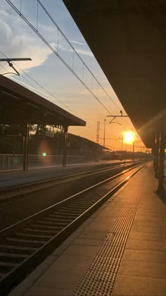 the sun is setting at an empty train station