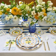 the table is set with blue and white plates, silverware, and flowers in vases