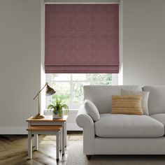 a living room with a couch, coffee table and window covered in pink roman shades