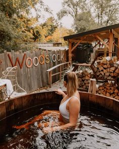 a woman in a hot tub with wood stock sign on the back wall and firewood stacked behind her