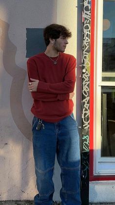 a man standing in front of a building with his arms crossed and leaning against the wall