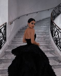 a woman in a black dress sitting on some stairs