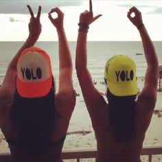 two women wearing hats with the word yolo written on them, standing in front of an ocean