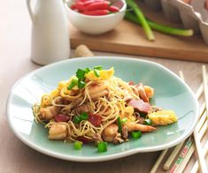 a white plate topped with noodles and meat on top of a wooden table next to chopsticks