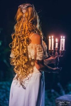 a woman with long hair holding candles in her hand