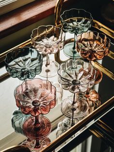 several wine glasses sitting on top of a glass shelf in front of a large mirror