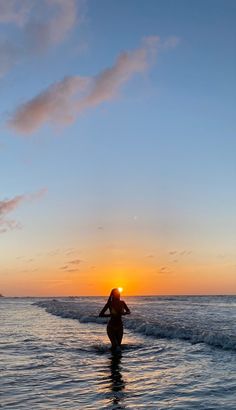 a woman walking into the ocean at sunset