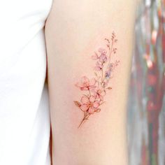 a small pink flower tattoo on the right arm and shoulder, with delicate flowers growing out of it