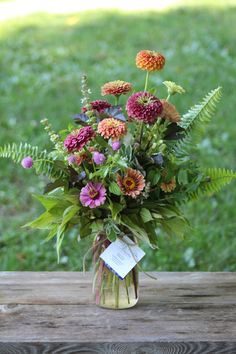 a vase filled with lots of flowers sitting on top of a wooden table next to grass