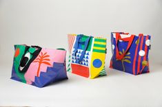 three brightly colored shopping bags sitting on top of a white table next to each other