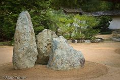 two large rocks sitting in the middle of a dirt area next to trees and bushes