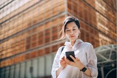 a woman standing in front of a building looking at her cell phone