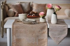 the table is set with two white vases and three pink roses