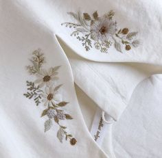 two white bedspreads with embroidered flowers and pine cones on them, laying next to each other