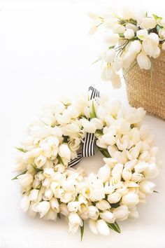 a wreath with white flowers on it next to a basket filled with tulips