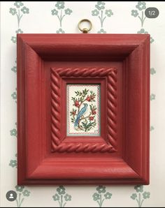 a red frame with a blue bird on it and green flowers in the back ground