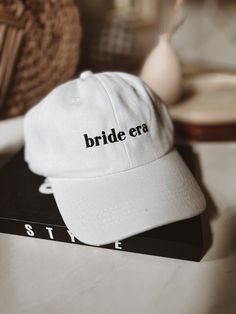 a white hat with the word bride era on it sitting next to a stack of books