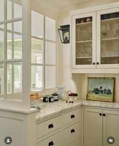 a kitchen with white cabinets and marble counter tops in front of a painting on the wall