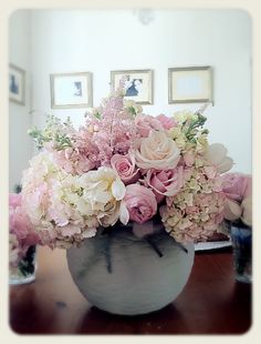 a vase filled with pink and white flowers sitting on top of a wooden table next to framed pictures