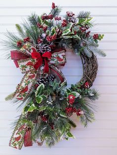 a christmas wreath with pine cones, holly and red ribbon hanging on a white wall