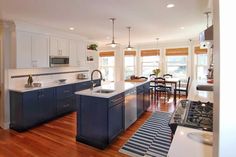 a kitchen with an island, stove and sink next to a dining room table in front of two windows