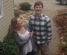 a young man and woman standing in front of a house smiling at each other's eyes