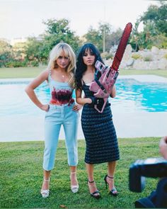 two women standing next to each other with a chainsaw on their shoulder and one holding a camera