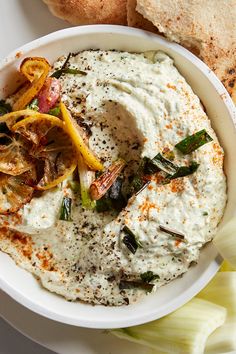 a white bowl filled with hummus and vegetables next to some bread on a plate