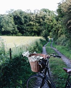 a bicycle parked on the side of a dirt road next to a lush green field