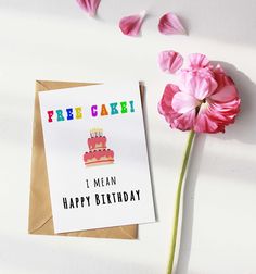 a card with a birthday cake on it next to pink flowers and a brown envelope