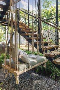 a swing chair with pillows on it in front of some stairs and plants, next to a set of steps that lead up to the second floor