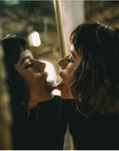 two young women are kissing each other in front of a glass window with their mouths open