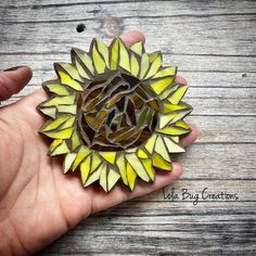 a hand holding a sunflower brooch in it's right hand on a wooden surface