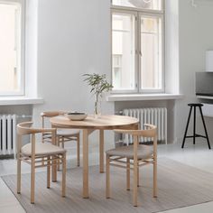 a table and chairs in a white room with two large windows on the opposite wall