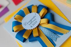 a blue and yellow bow on top of a card with congratulations written in it's center