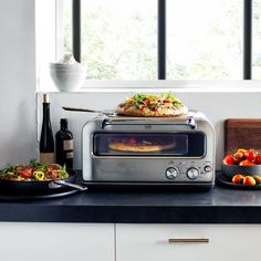 a toaster oven sitting on top of a counter next to bowls of fruit and vegetables