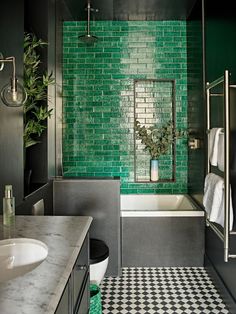 a green tiled bathroom with black and white checkered flooring on the shower wall