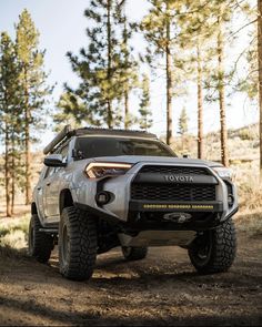 the front end of a white toyota truck parked on a dirt road in the woods