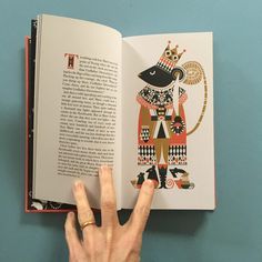 the hand is pointing at an open book with illustrations on it, which includes a stylized image of a mouse